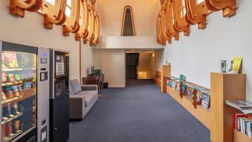 A hotel lobby with a vending machine, a sofa, a staircase, and a bookshelf with books.