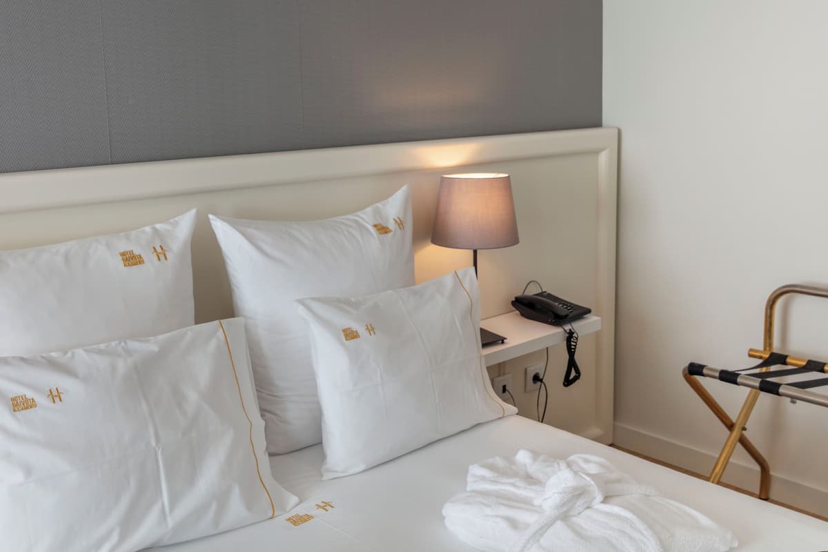 A hotel room with a neatly made bed, a bedside lamp, a telephone, and an ironing board.
