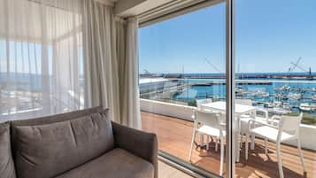 A balcony with a view of a marina, a white table and chairs, and a grey sofa.