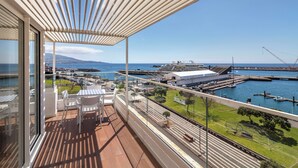 Un balcón con vista a un puerto deportivo, barcos y una cordillera distante.