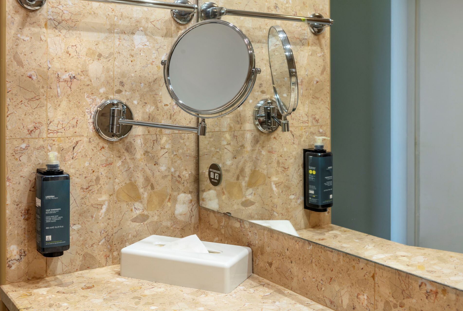 Un baño con encimera de mármol, un espejo, dispensador de toallas y dos botellas de loción.