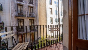 A balcony with a wooden table and chairs, a metal railing, and a view of adjacent buildings. - Hostal Hera (Barcelona)