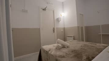 Een hotelkamer met een bed, een wandlamp, een radiator en een deur.