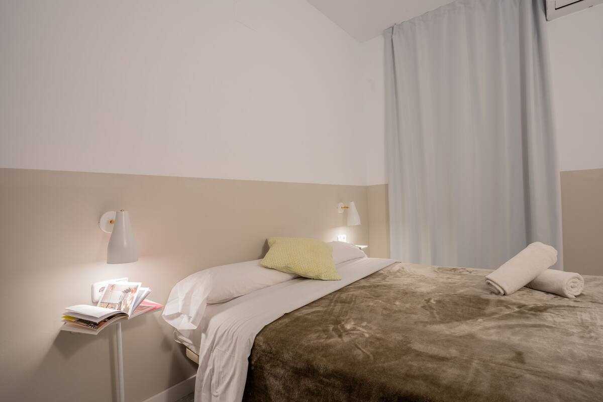 A hotel room with a bed, a nightstand, a lamp, and a window with curtains.