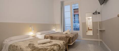 A hotel room with two beds, a TV mounted on the wall, a window with a view of a balcony, and a mirror on the wall.