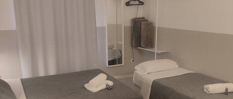 Habitación de hotel con dos camas individuales, un televisor montado en la pared, un espejo y una ventana con cortinas.