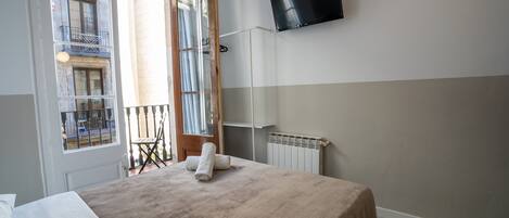 Quarto de hotel com cama, televisão fixada na parede, janela com vista para edifícios e radiador.