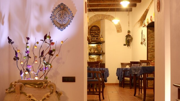 A rustic interior with a wooden staircase leading to a dining area, a large decorative vase with branches, and a brick archway. - Le Cinque Novelle (Agrigento)