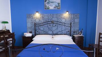 Ein Hotelzimmer mit blauer Wand, einem Bett mit Metallkopfteil, zwei Nachttischen mit Lampen, einem Bild an der Wand und Blick auf eine Landschaft.