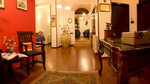 A hallway with a wooden floor, a red wall, and a large vase with flowers. There is a chair and a table with a book on it. - Le Cinque Novelle (Agrigento)