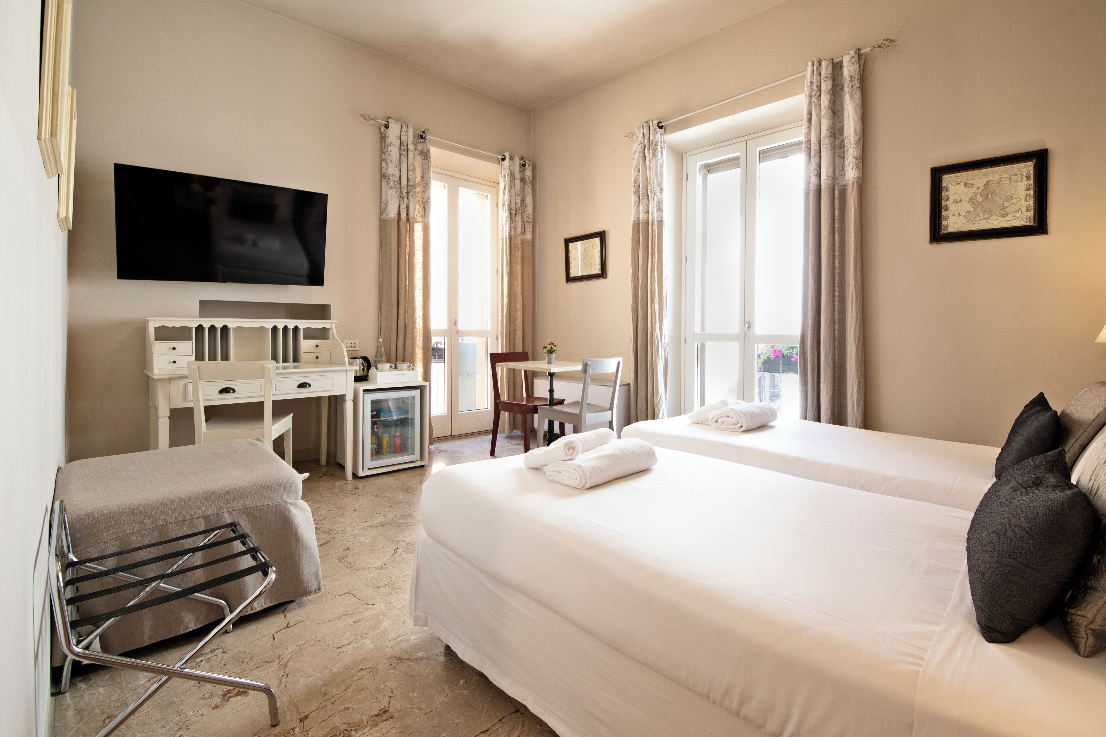 Habitación de hotel con dos camas, un escritorio, una silla, un televisor y una ventana con cortinas.
