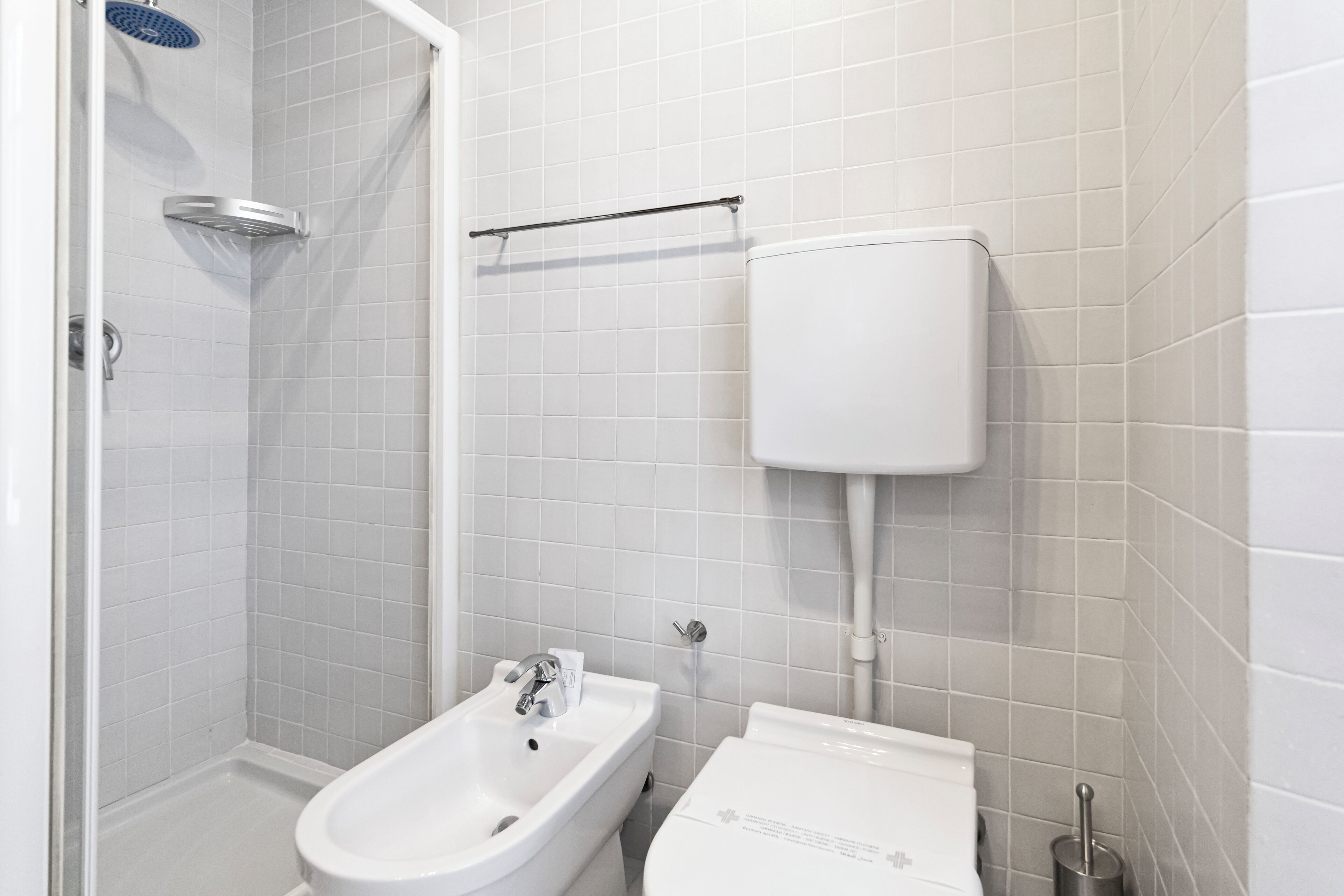 Un baño con azulejos blancos, ducha, lavabo e inodoro.