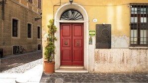 A red door with a small potted plant beside it, a street lamp above, and a sign indicating a hotel. - Hotel Broletto Mantova - centro storico (Mantua)