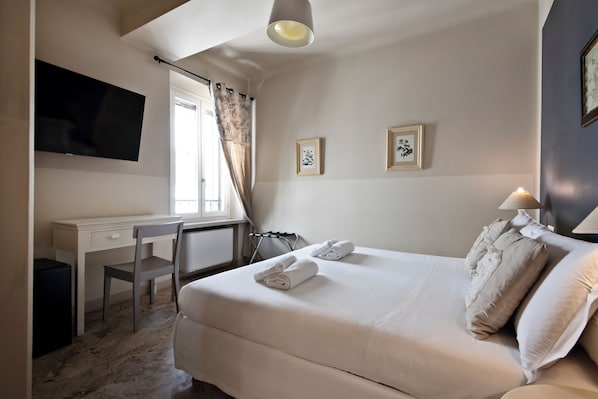 A hotel room with a bed, a desk, a chair, a TV, and two framed pictures on the wall. - Hotel Broletto Mantova - centro storico (Mantua)