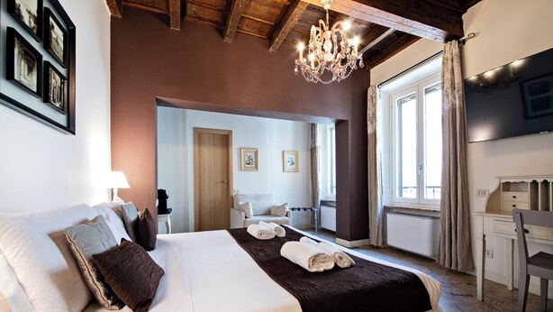 A well-lit bedroom with a large bed, a desk, and a chair, featuring a chandelier and framed pictures on the wall. - Hotel Broletto Mantova - centro storico (Mantua)