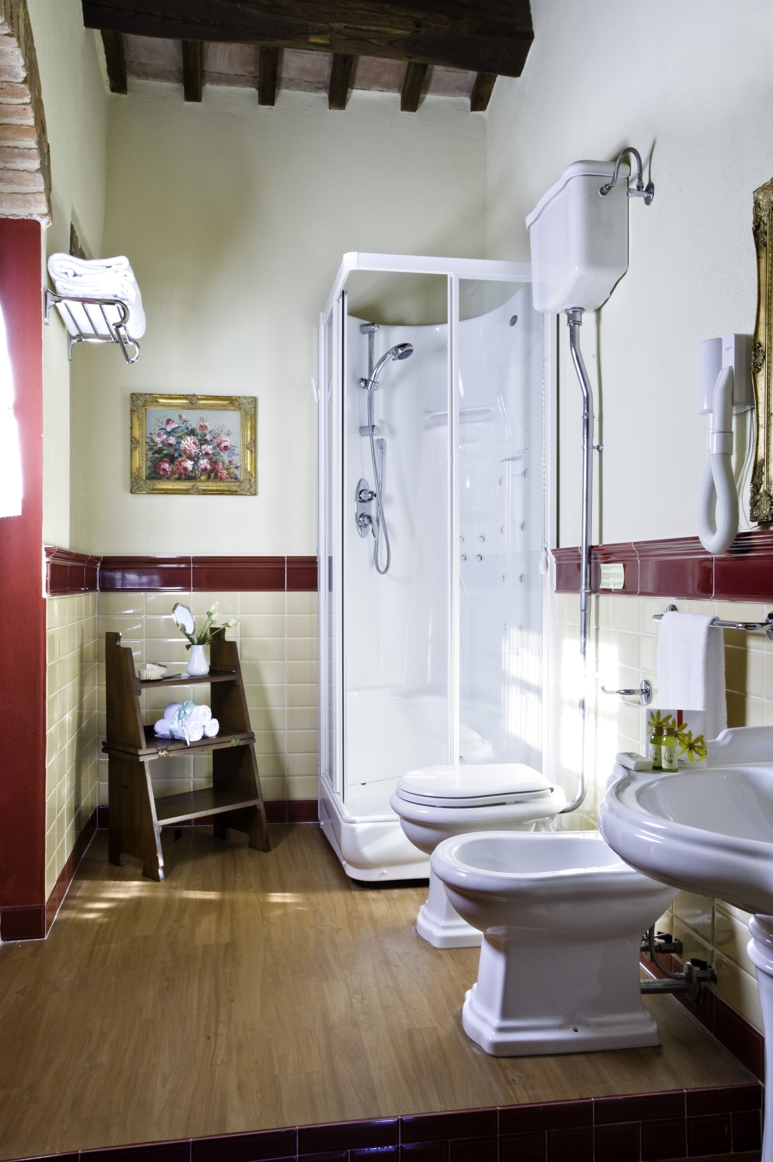 A bathroom with a shower enclosure, two toilets, a sink, and a towel rack.