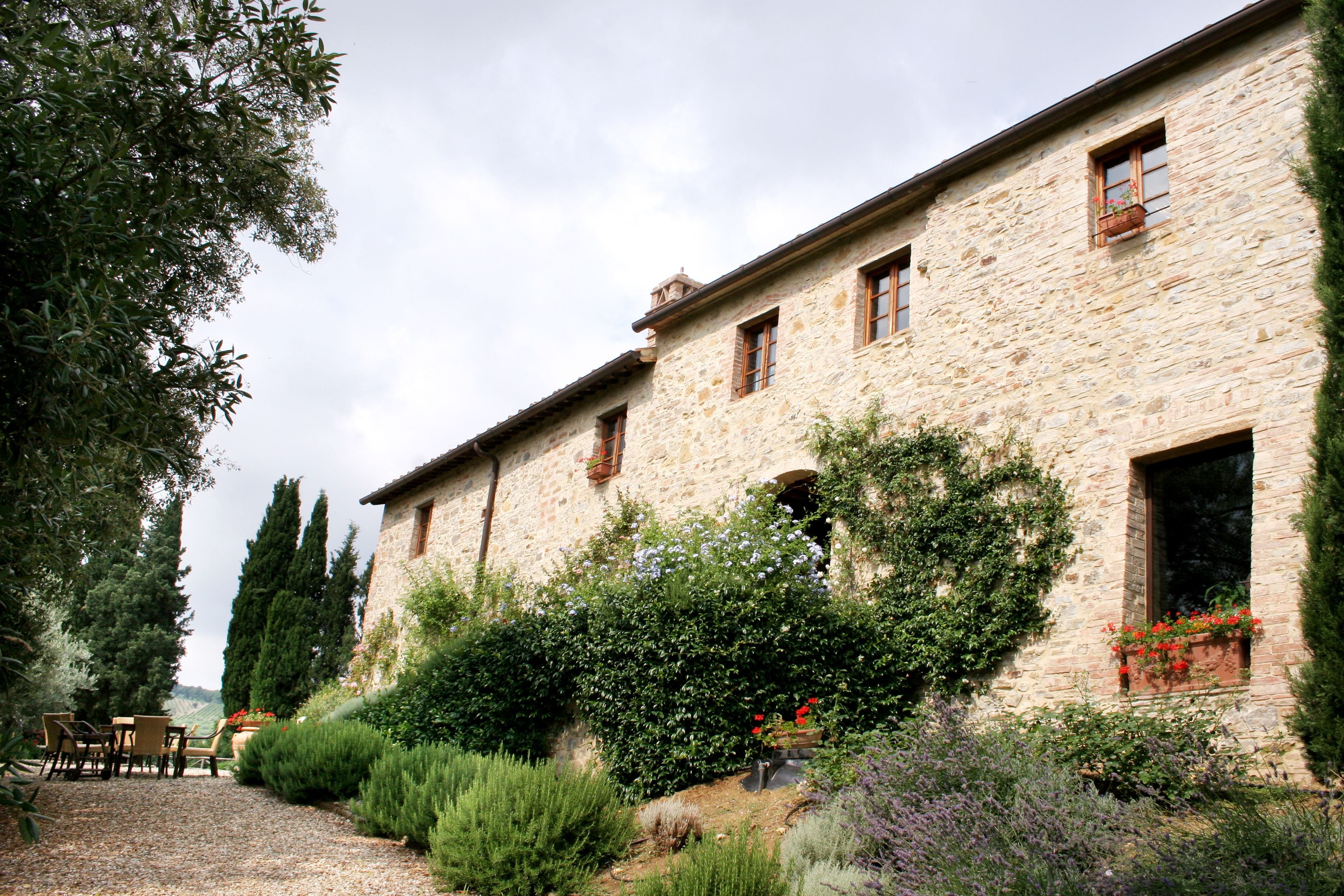 Un edificio in pietra con molte finestre, immerso nel verde e con un vialetto ghiaioso.