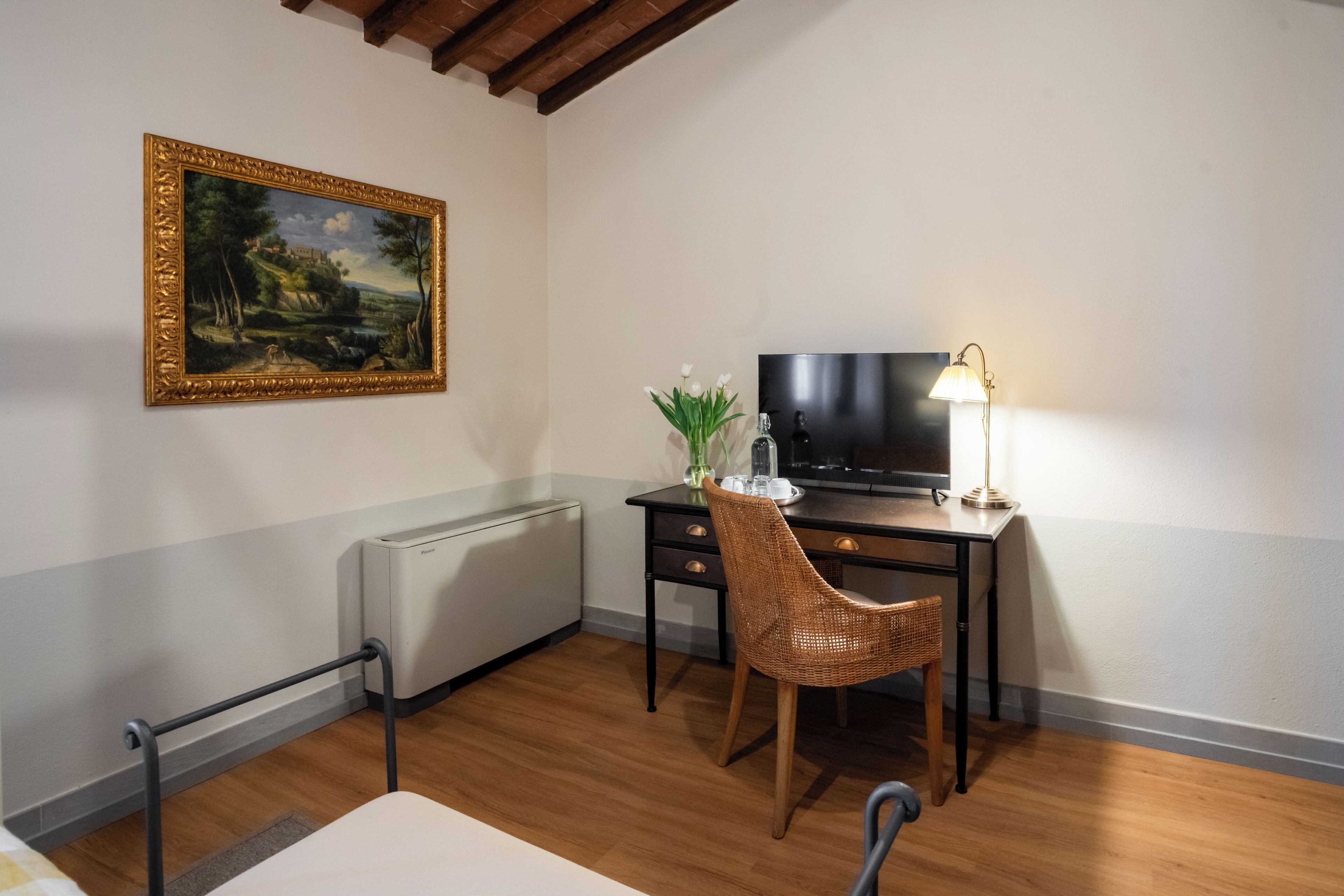 Ein Zimmer mit einem Bett, einem Schreibtisch mit Lampe, einem Fernseher, einer Heizung und einem gerahmten Gemälde an der Wand.