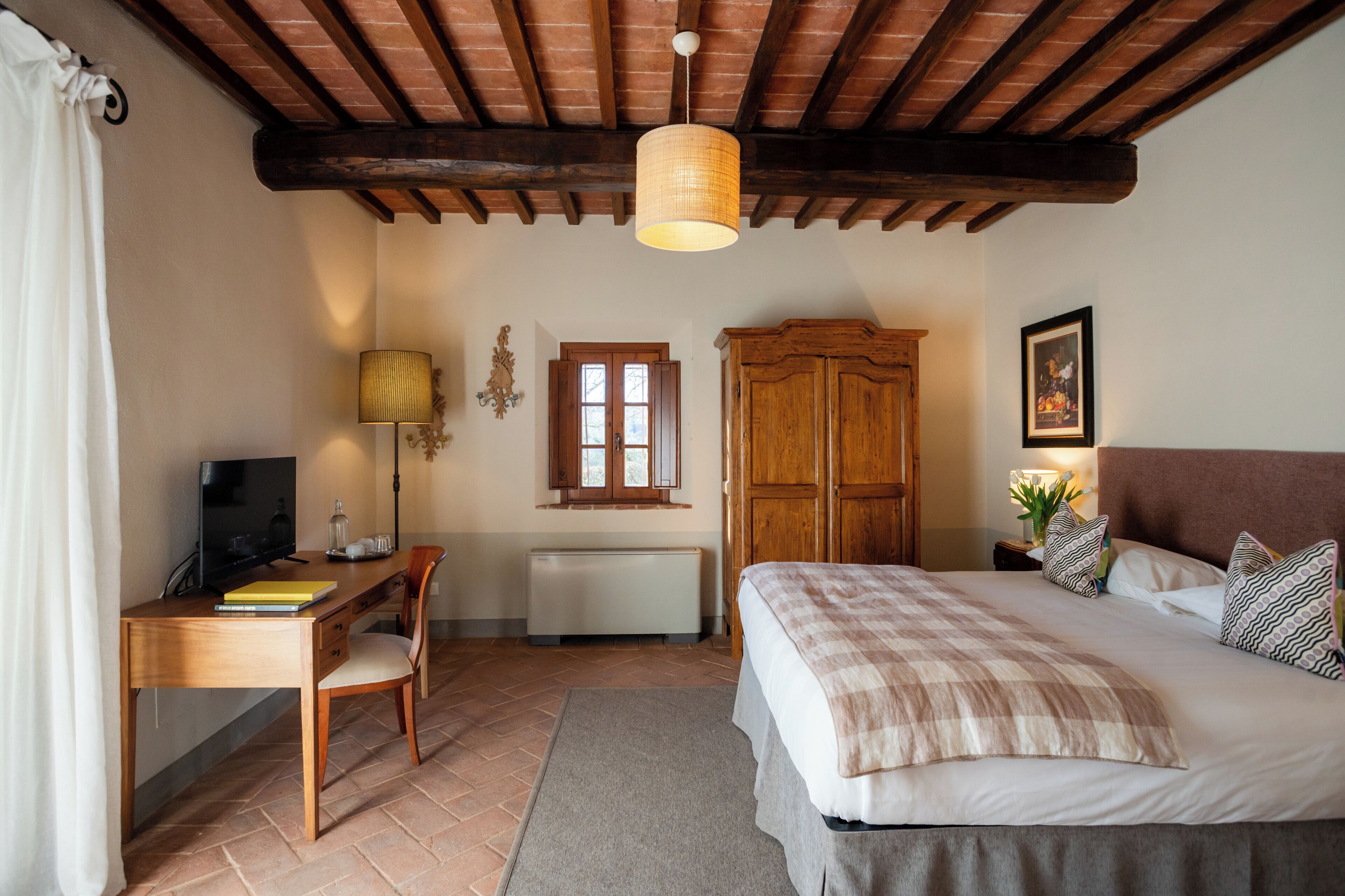 Un dormitorio con una cama, un escritorio, una silla, un radiador, un armario de madera y una lámpara colgante.