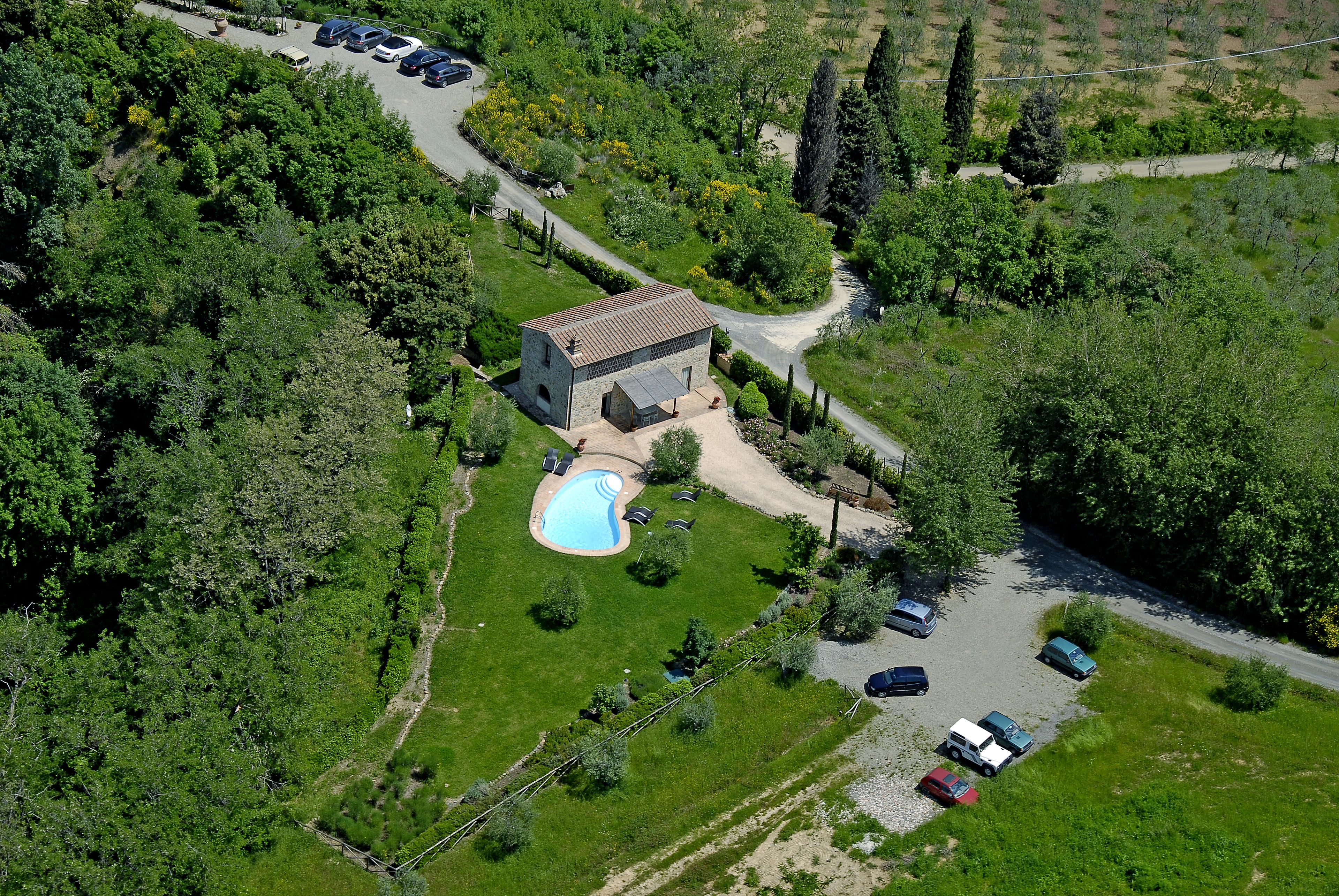 An aerial view of a property with a swimming pool, a small building, and several parked cars.