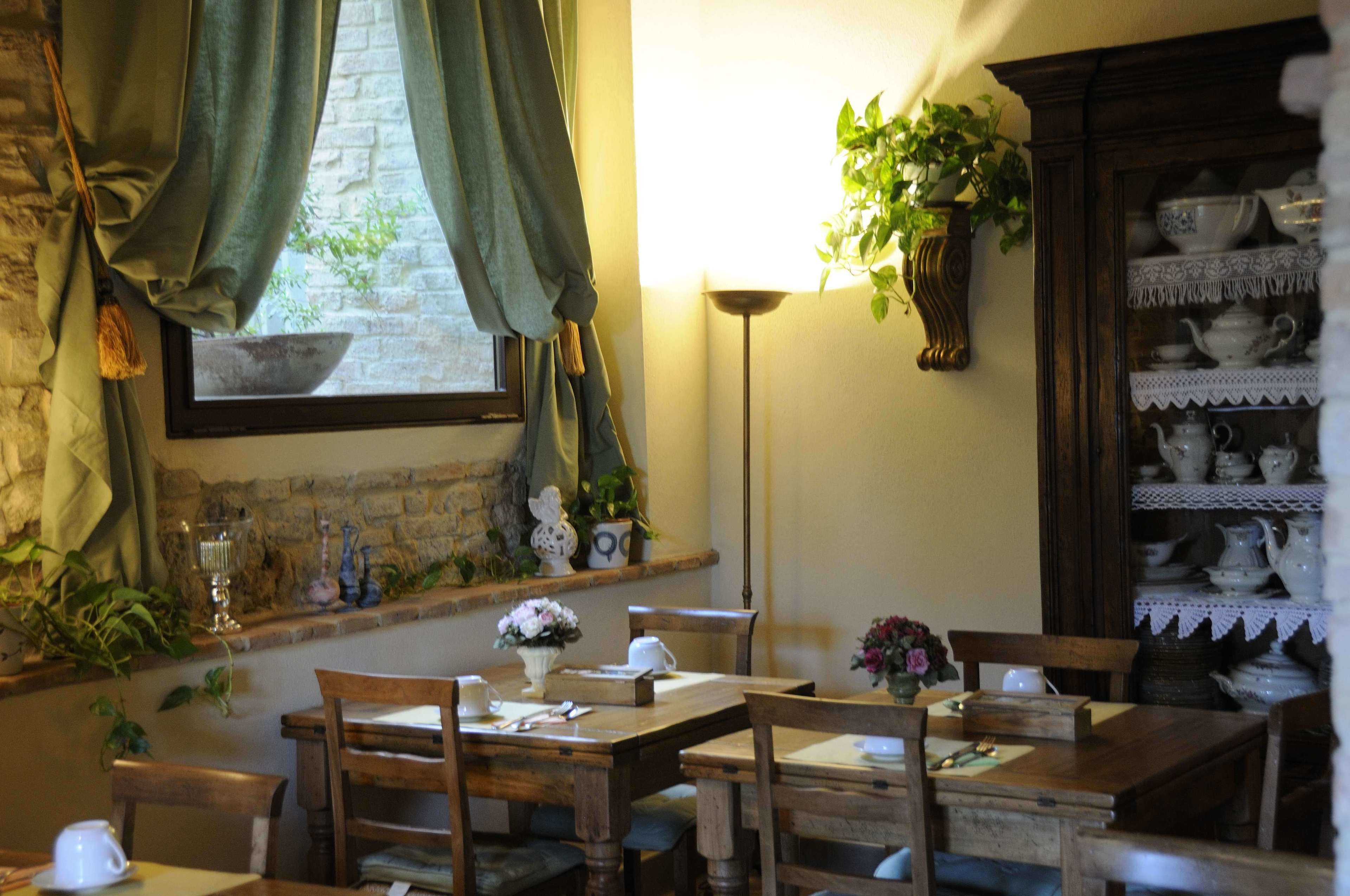 A dining area with wooden furniture, a window with curtains, a lamp, and a shelf with dishes.