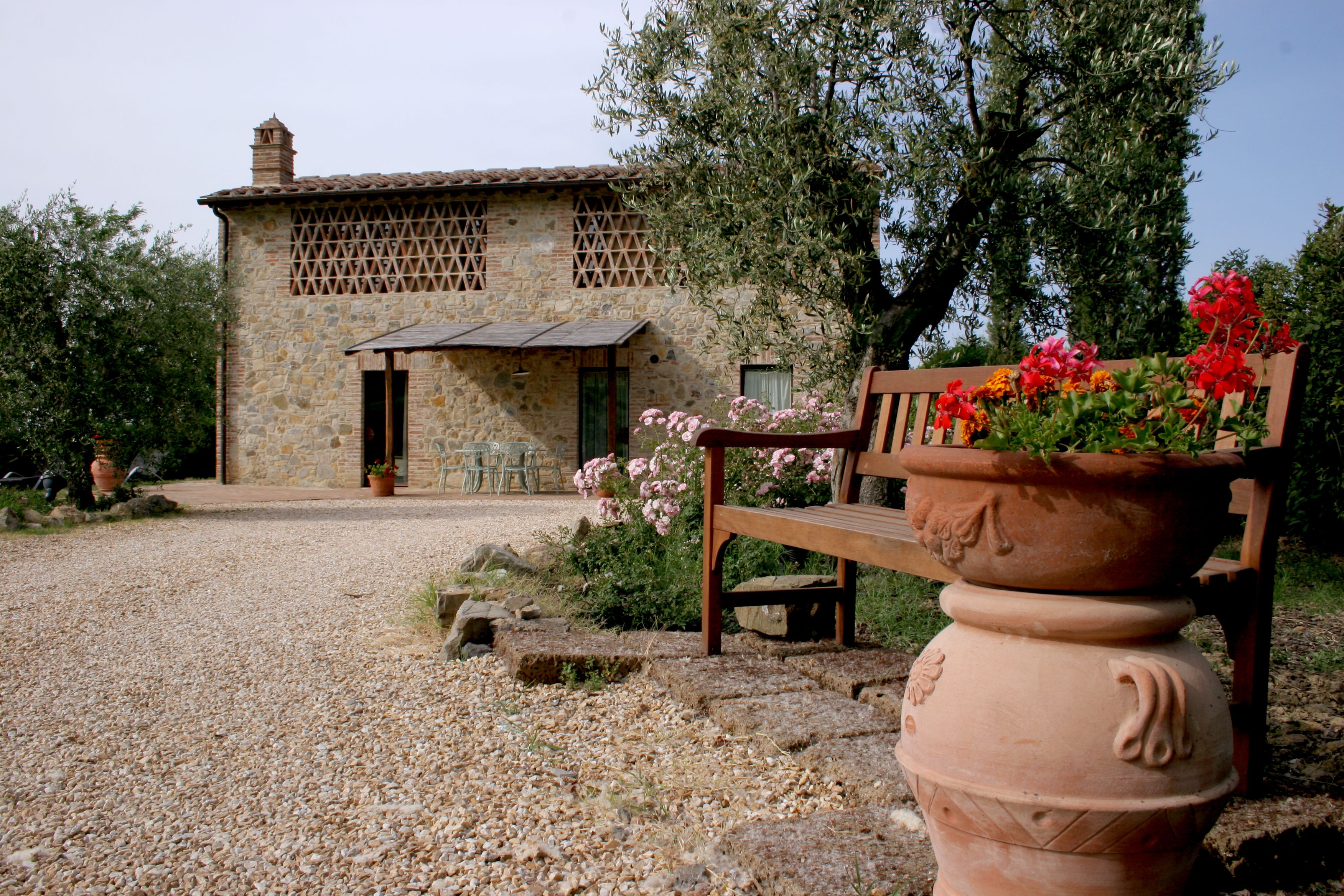Un bâtiment en pierre avec un toit en tuiles, un banc et un grand pot en terre cuite rempli de fleurs.