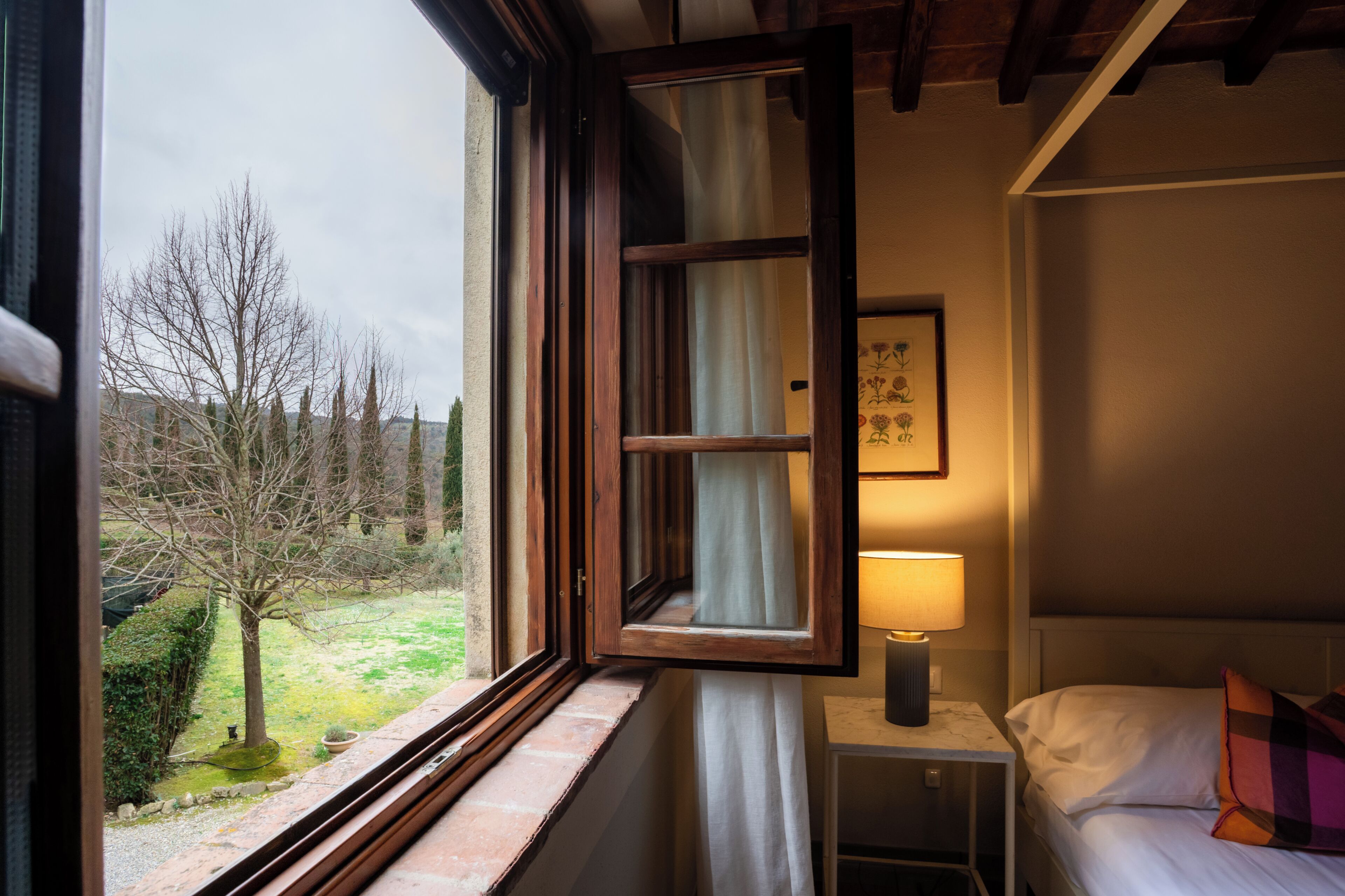 Un dormitorio con ventana, lámpara de noche, cama y mesita de noche.