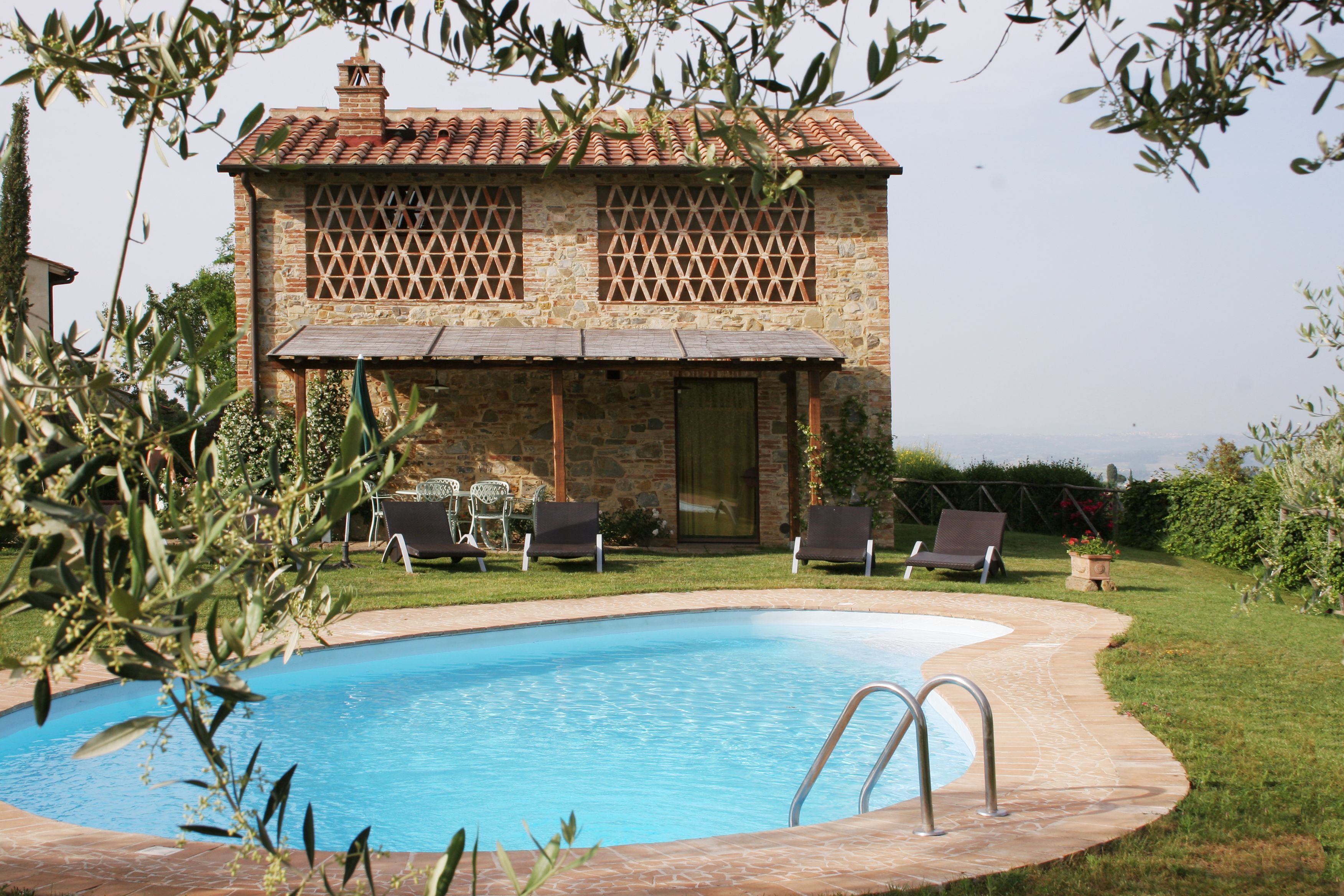 A stone building with a pool, surrounded by greenery and two lounge chairs.