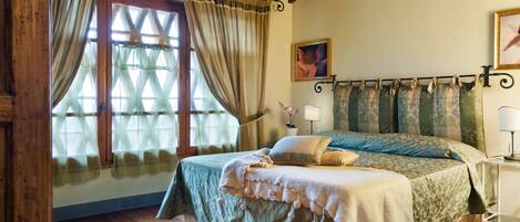 A bedroom with a wooden ceiling, a bed with a green bedspread, a window with curtains, and a bedside table with a lamp.