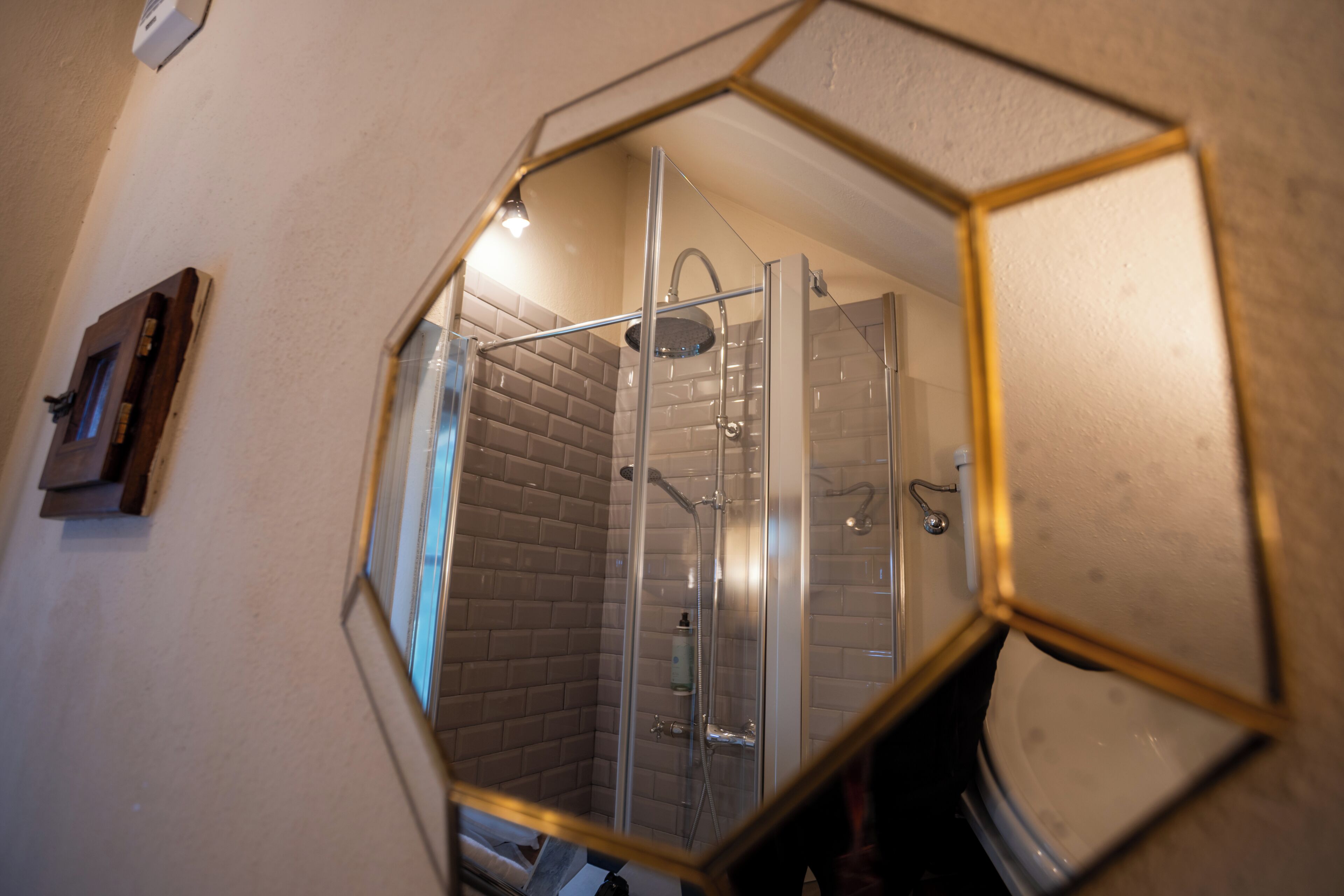 A bathroom with a glass shower enclosure, a visible toilet, and a mirror with a geometric frame.