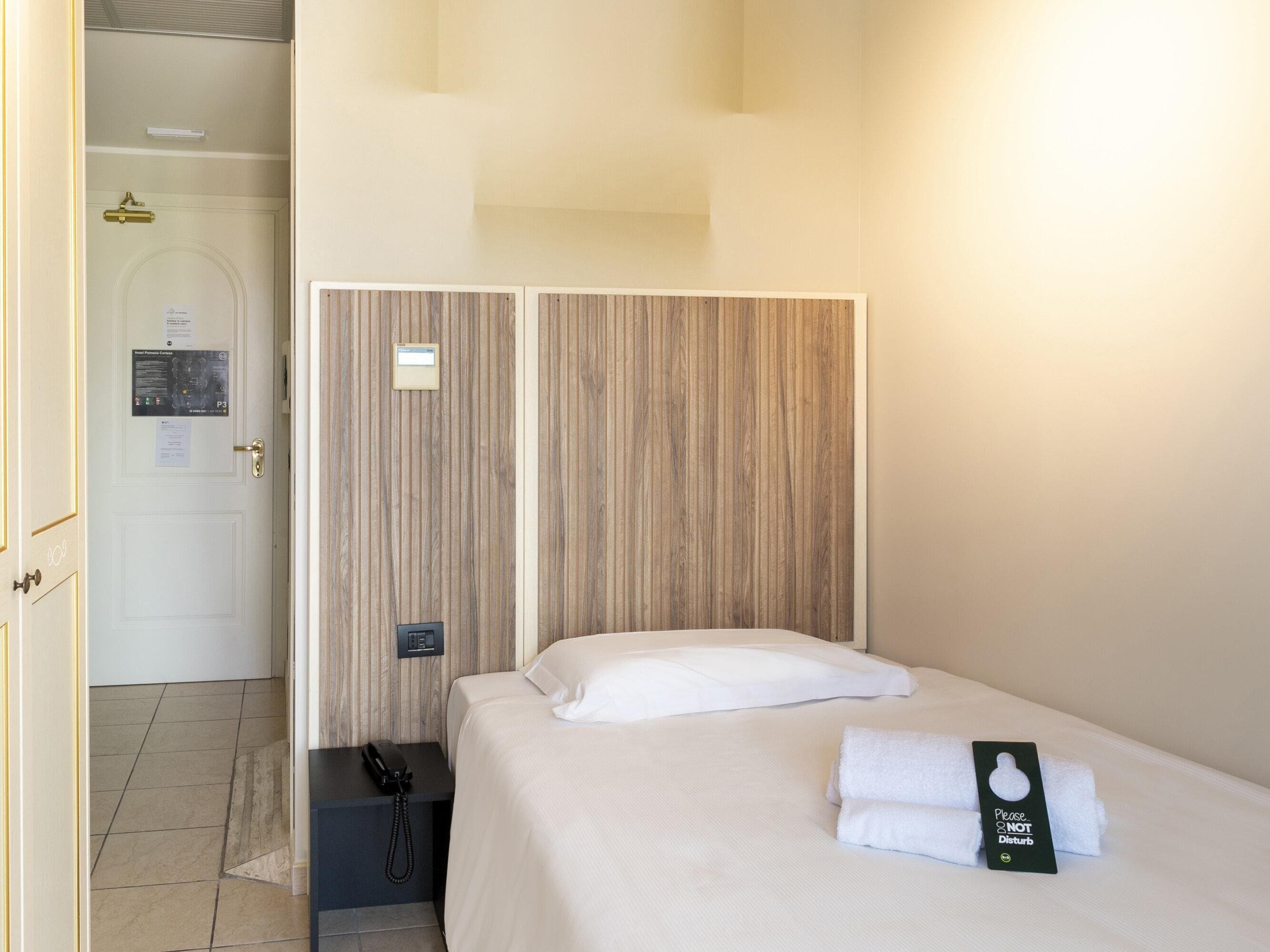 Habitación de hotel con cama, teléfono en la mesita de noche y toalla con el letrero 'No molestar'.