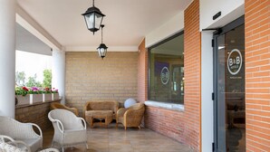 A covered outdoor seating area with wicker chairs, a hanging lantern, and a brick wall. - B&B Hotel Pomezia Cortese (Pomezia)