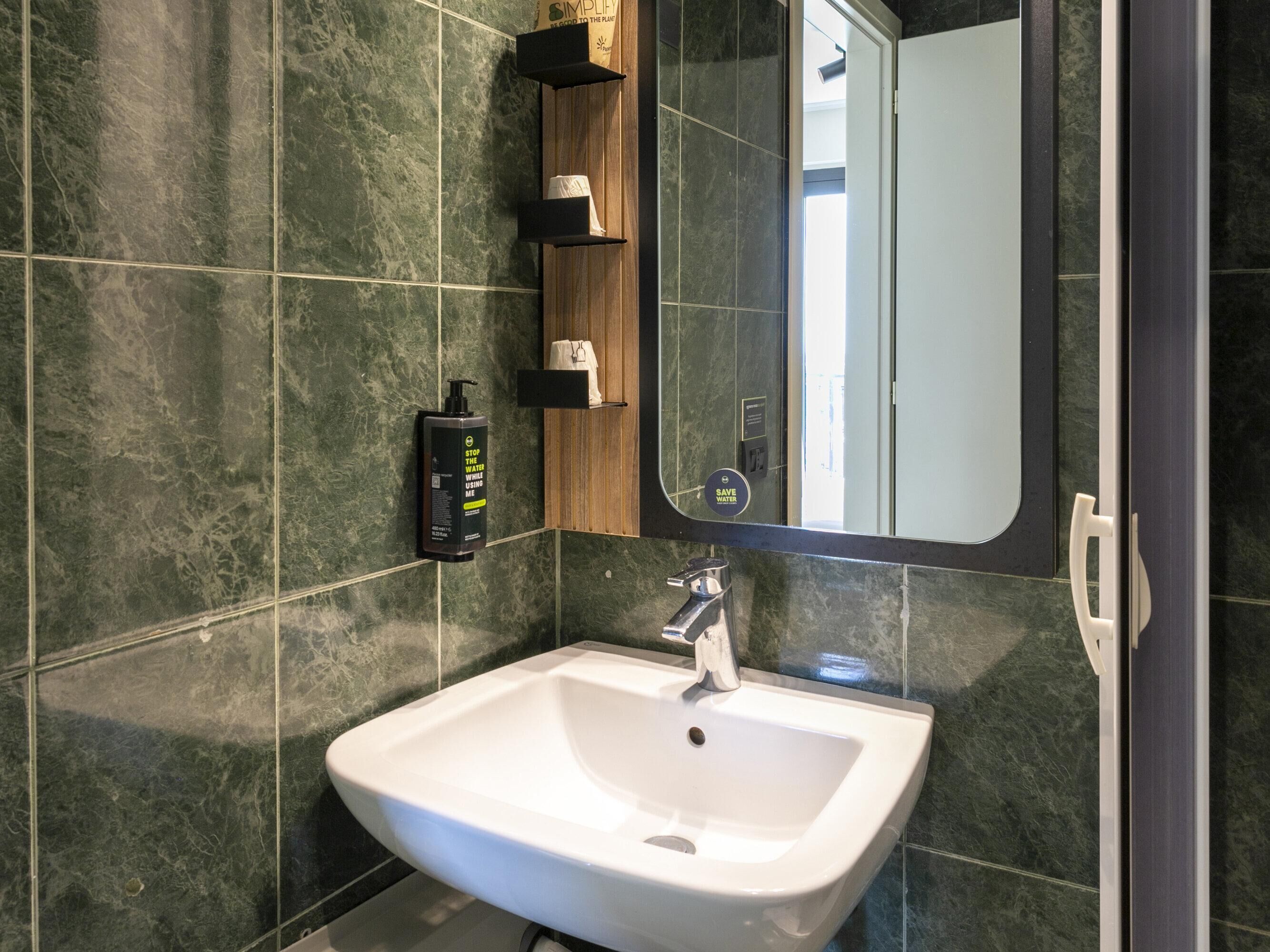 Un bagno moderno con un lavandino bianco, uno specchio e un erogatore di sapone a parete.
