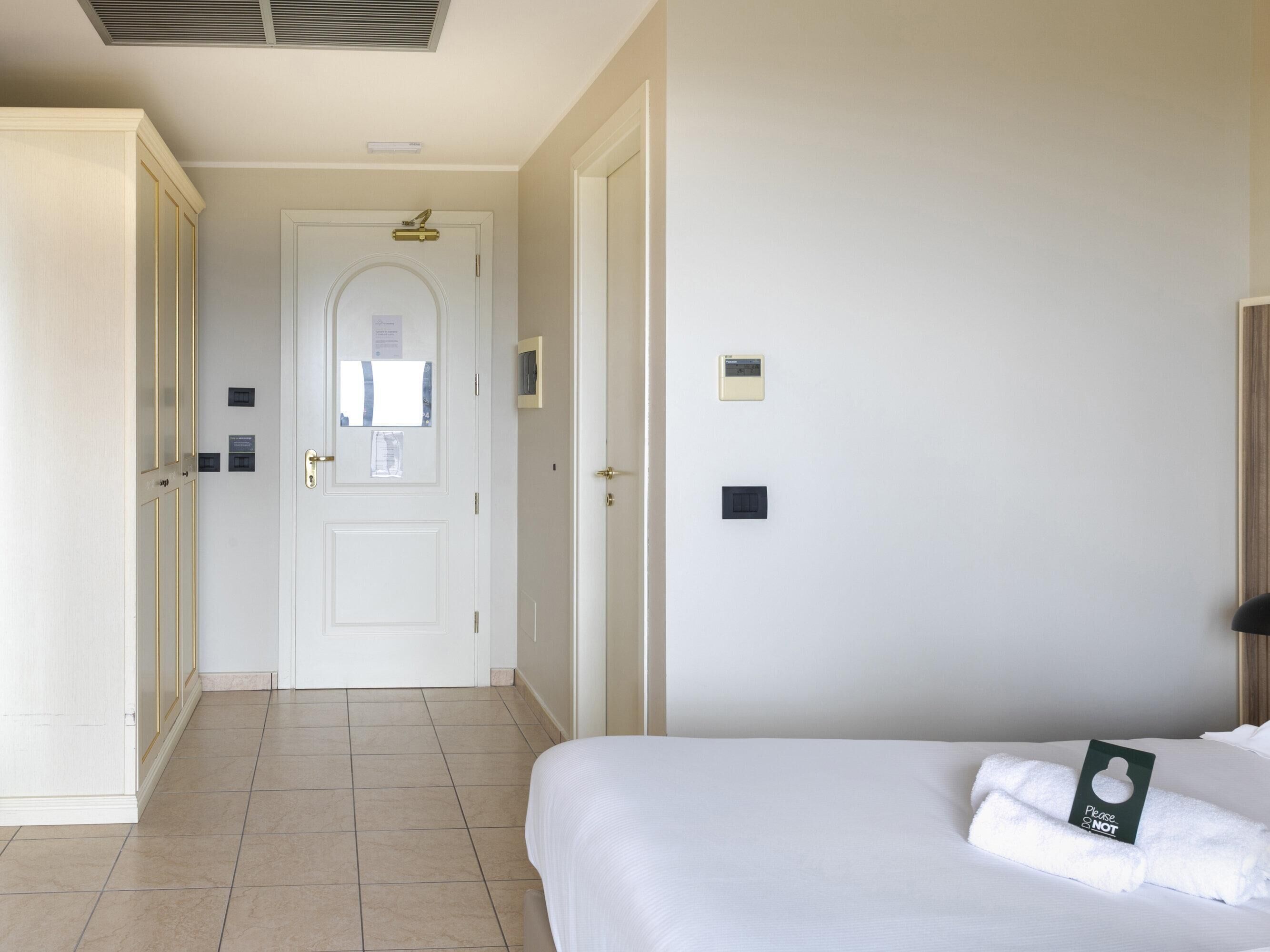 Ein Hotelzimmer mit einem Bett, einem Kleiderschrank, einer Tür mit Griff und einem wandmontierten Thermostat.