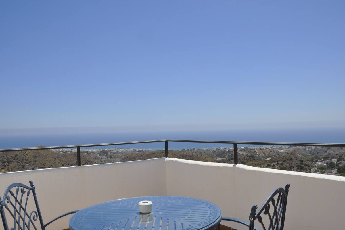 A balcony with a table and chairs, overlooking a coastal landscape.