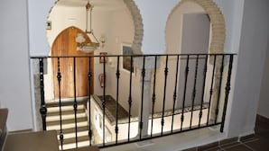 A staircase with a black metal railing, leading to an interior space with a wooden door and a chandelier. - Hotel Mamabels (Mojacar)