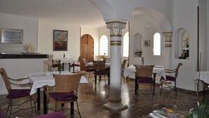 A restaurant with white walls, wooden tables, and chairs. There are arches and columns in the room. - Hotel Mamabels (Mojacar)