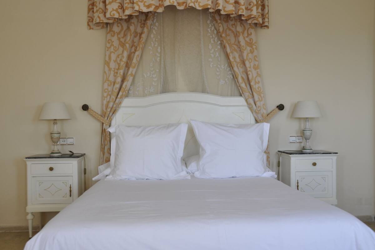 A neatly made bed with white linens, two bedside tables with lamps, and a patterned curtain above the headboard.