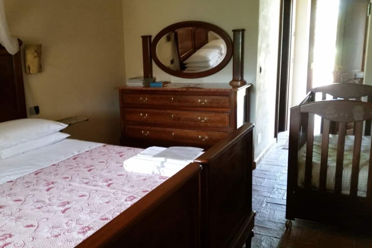 Een slaapkamer met een bed, een houten dressoir, een spiegel en een ledikant.