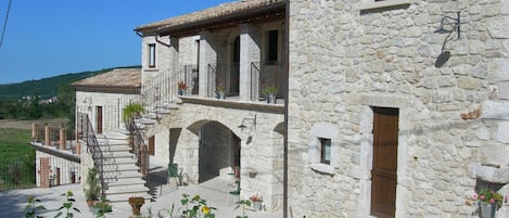 Un edificio de piedra con un balcón, una escalera y un jardín con flores y una bicicleta.