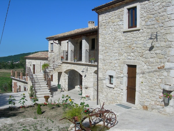 A stone building with a balcony, a staircase, and a garden with flowers and a bicycle.