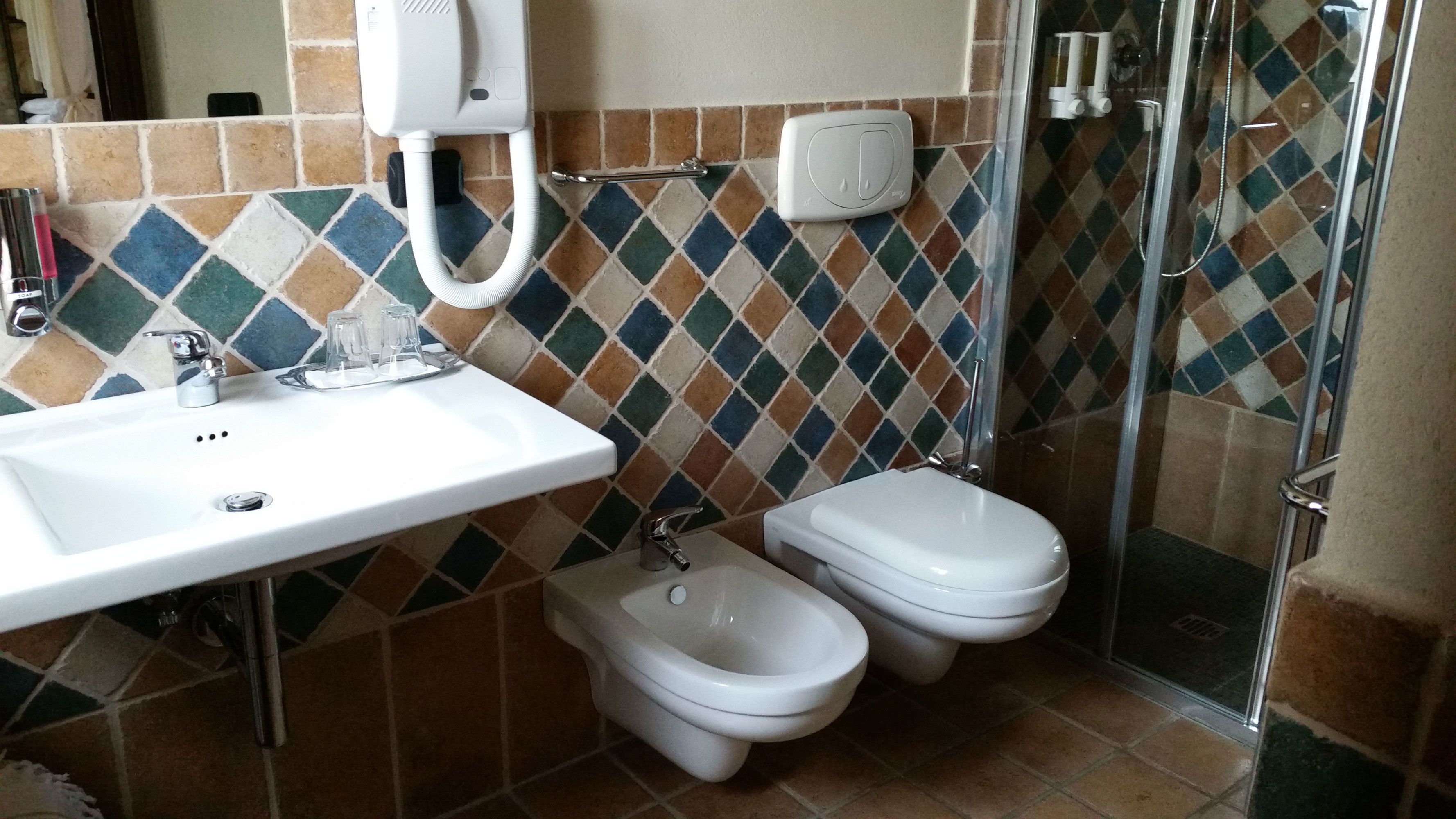 Een badkamer met een witte wastafel, twee toiletten, een bidet en een douchecabine.