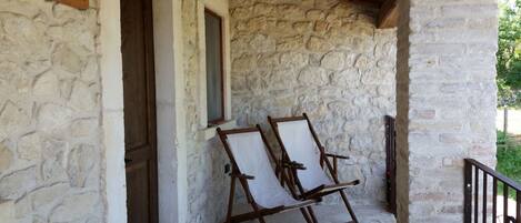 Habitación con paredes de piedra, dos sillas de madera y una puerta de madera con la etiqueta 'PEGASC'.