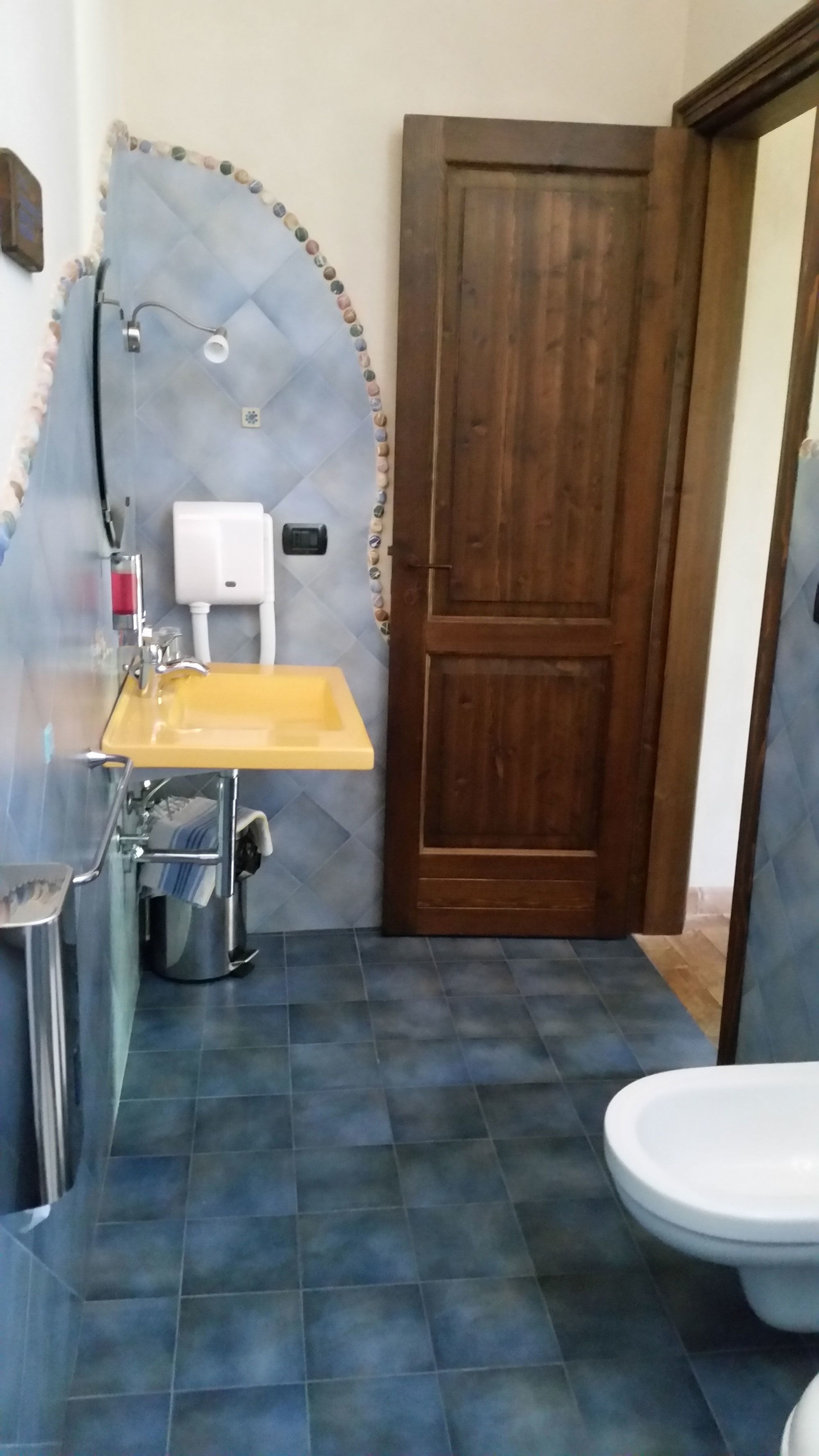 A bathroom with a wooden door, a yellow sink, a white toilet, and a blue-tiled floor.