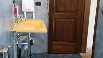 Un baño con puerta de madera, lavamanos amarillo, inodoro blanco y suelo de azulejos azules.