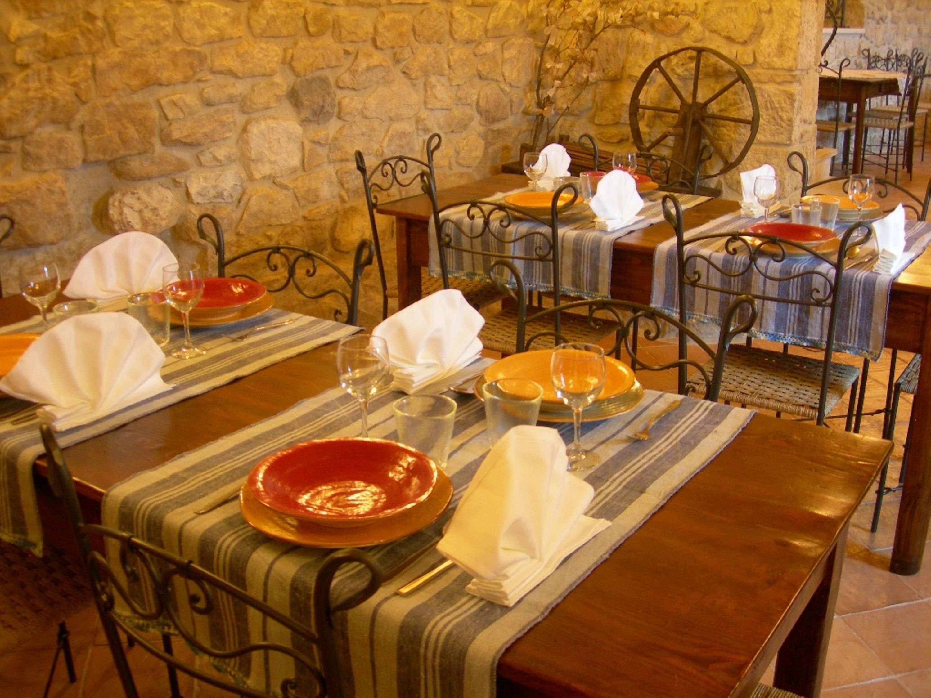 Un comedor con paredes de piedra, sillas de metal y mesas dispuestas con platos, vasos y servilletas.