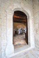 Habitación con paredes de piedra, una cama bajo techo de madera, suelo de piedra y un arco de piedra.