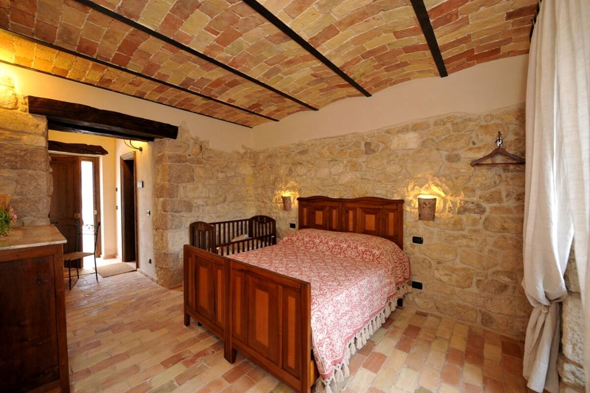 Een slaapkamer met een houten bed, stenen muren en een schuin plafond.