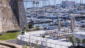 A marina with numerous boats docked, a stone wall, and a seating area with umbrellas.