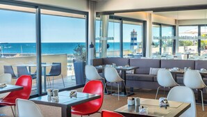 A modern restaurant with large windows offering ocean views, a seating area with a sofa and tables, and a casual dining setup.